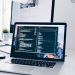 Laptop displaying source code in a dark developer workspace, representing AI-assisted coding tools