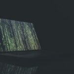 Dark illustration of cascading green code on a laptop screen, symbolizing cybersecurity and on-device threat detection